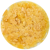 A circular close-up of fine yellow Carnauba wax flakes or shavings filling the frame, photographed on a white background.