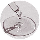 A close-up circular shot of a clear glass dropper above a glossy puddle of transparent liquid on a light textured surface.
