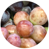 A close-up circular photo of several grapes, including pinkish-red and pale cream varieties with some darker purple grapes visible in the background.