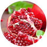 A close-up circular photo of a cut pomegranate showing bright red arils and white pith, with additional whole pomegranate pieces and green leaves in the background.