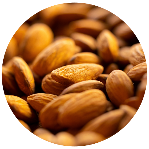 A close-up circular photo of whole almonds piled together, with warm golden-brown tones and shallow depth of field.