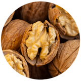 A close-up circular photo of several walnuts, with one walnut cracked open in the center showing the pale beige brain-like interior and brown shell around it.
